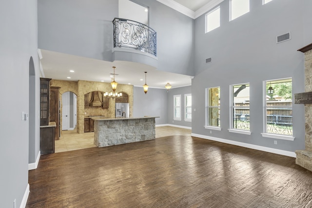 unfurnished living room with a high ceiling, light hardwood / wood-style floors, ornamental molding, and a notable chandelier