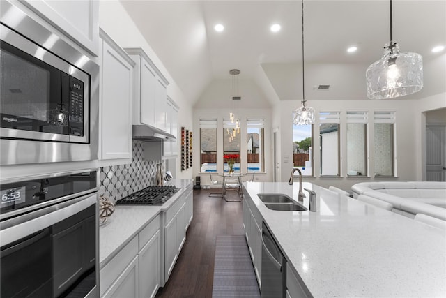 kitchen featuring light stone counters, tasteful backsplash, lofted ceiling, appliances with stainless steel finishes, and a sink