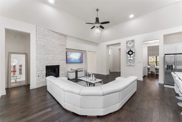 living area featuring a ceiling fan, dark wood-style flooring, a stone fireplace, and baseboards