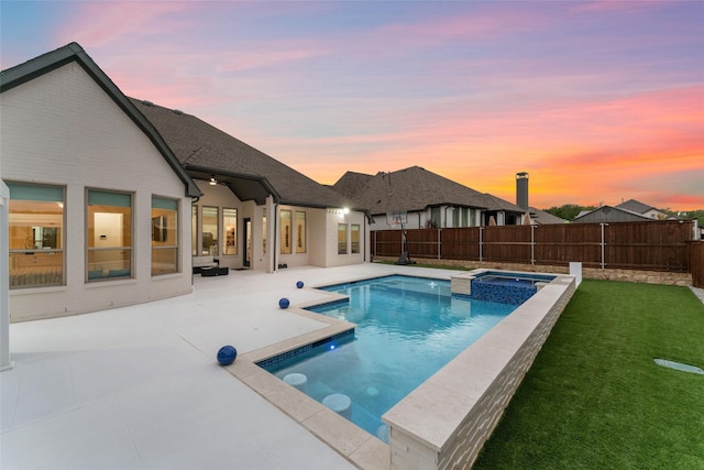 pool at dusk featuring a yard, a patio area, a fenced backyard, and a pool with connected hot tub