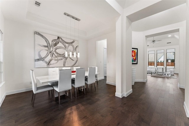 dining room with a raised ceiling, ceiling fan, and dark wood-type flooring