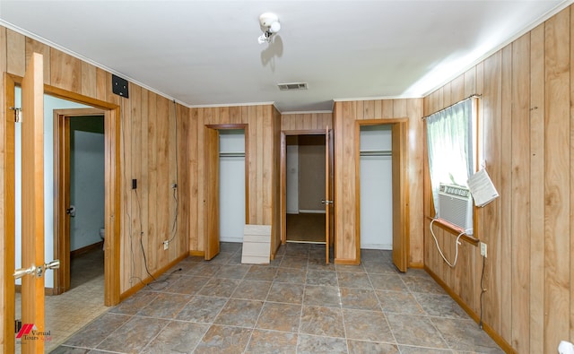 unfurnished bedroom featuring wooden walls, two closets, and crown molding