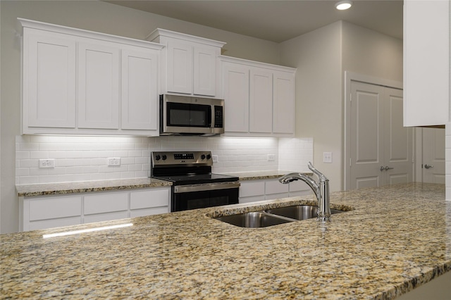 kitchen with light stone countertops, sink, white cabinets, backsplash, and stainless steel appliances