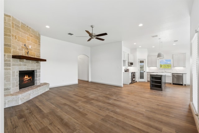 unfurnished living room featuring a stone fireplace, beverage cooler, ceiling fan, hardwood / wood-style flooring, and sink