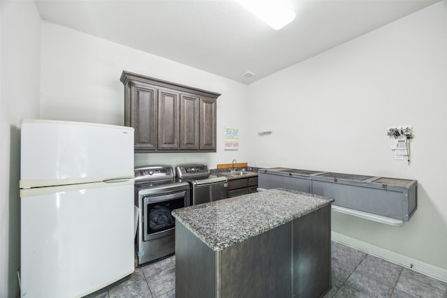 kitchen with stone countertops, sink, a center island, white fridge, and washing machine and dryer