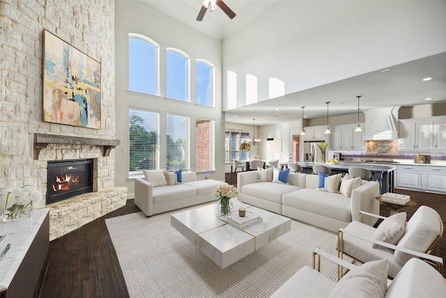 living room featuring a high ceiling, a stone fireplace, ceiling fan with notable chandelier, and light hardwood / wood-style floors