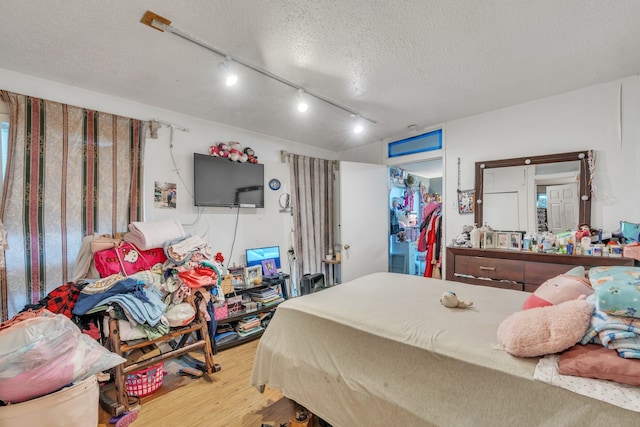 bedroom with a closet, light hardwood / wood-style floors, track lighting, and a textured ceiling