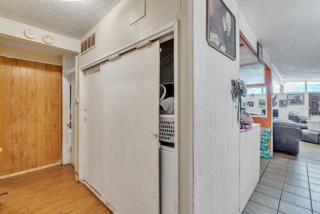 hall featuring light wood-type flooring, a textured ceiling, and wooden walls