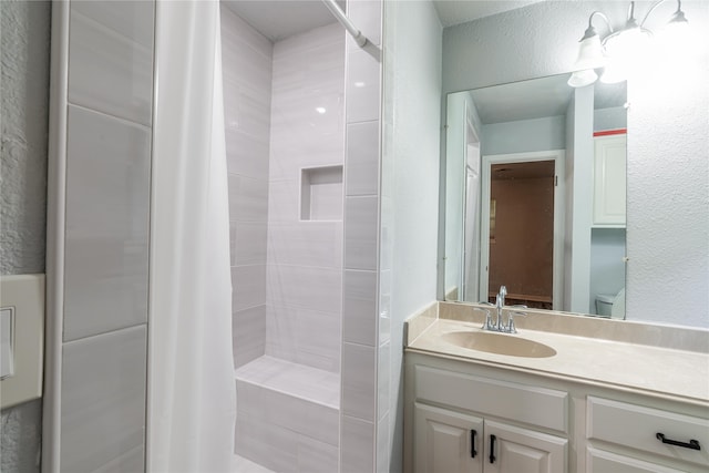 bathroom with a textured wall, a tile shower, and vanity