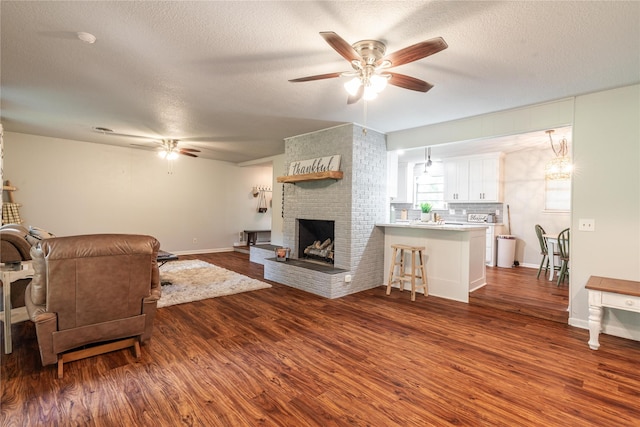 living area featuring a textured ceiling, wood finished floors, ceiling fan, and a brick fireplace