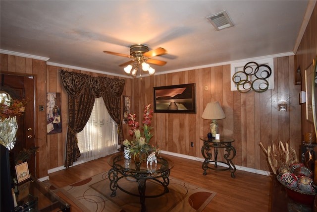 living room featuring wood walls, ornamental molding, hardwood / wood-style floors, and ceiling fan