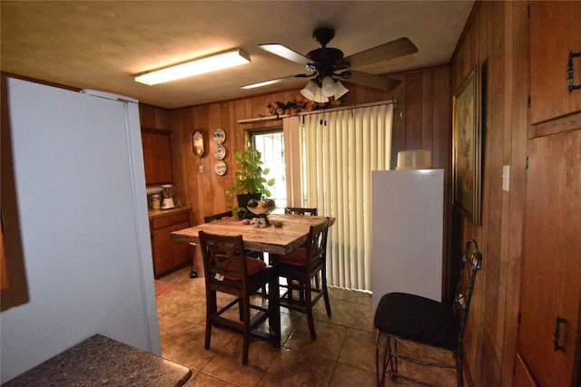 dining space featuring wood walls, ceiling fan, and tile patterned floors