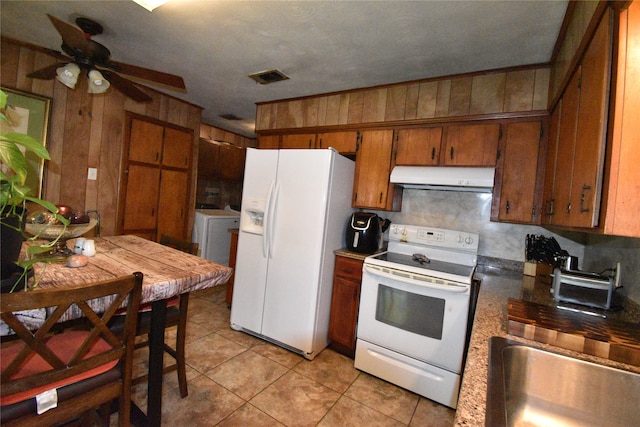 kitchen with wooden walls, white appliances, independent washer and dryer, light tile patterned floors, and ceiling fan