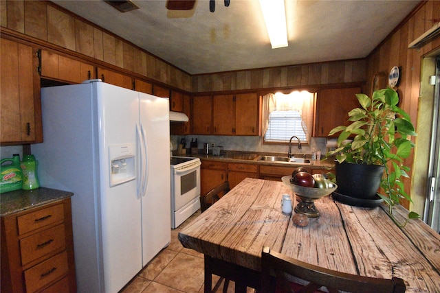 kitchen featuring light tile patterned flooring, sink, wooden walls, white appliances, and ceiling fan