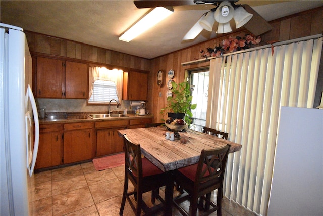 kitchen featuring light tile patterned flooring, white refrigerator, ceiling fan, wooden walls, and sink