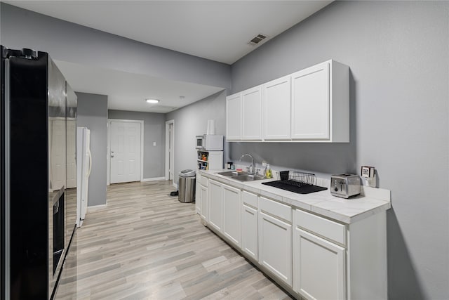 kitchen featuring light hardwood / wood-style floors, sink, white appliances, white cabinets, and tile counters