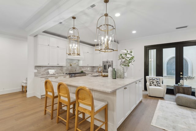 kitchen with decorative light fixtures, white cabinetry, appliances with stainless steel finishes, light stone countertops, and french doors