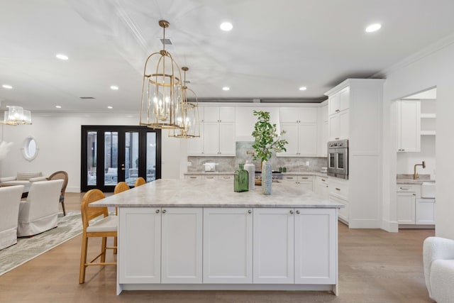 kitchen featuring a spacious island, white cabinetry, oven, light wood-type flooring, and crown molding