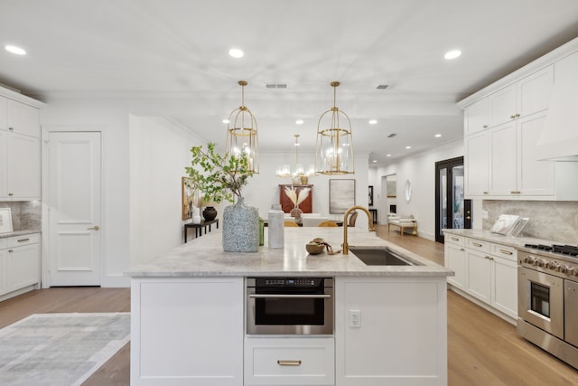 kitchen featuring stainless steel appliances, tasteful backsplash, a kitchen island with sink, hanging light fixtures, and sink