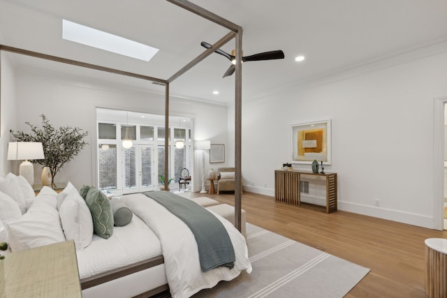 bedroom featuring ceiling fan, hardwood / wood-style floors, ornamental molding, and a skylight