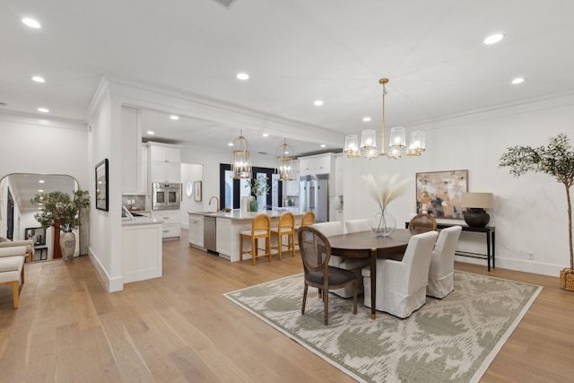 dining space with light wood-type flooring, a notable chandelier, sink, and ornamental molding