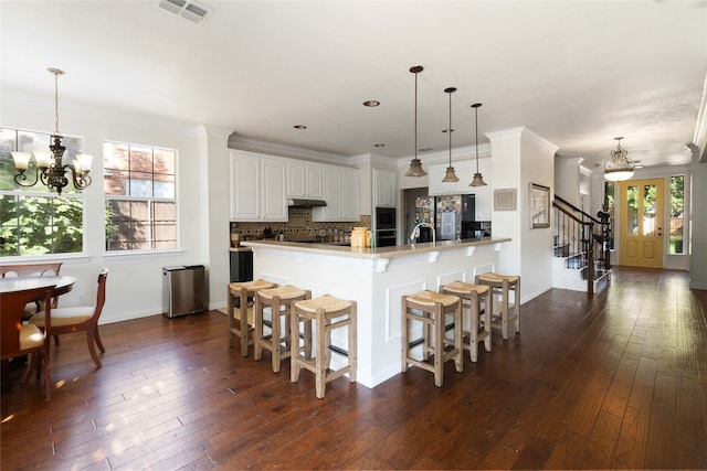 kitchen featuring dark hardwood / wood-style floors, a notable chandelier, white cabinetry, hanging light fixtures, and crown molding