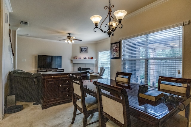 dining area with light colored carpet, ceiling fan with notable chandelier, ornamental molding, and a tile fireplace