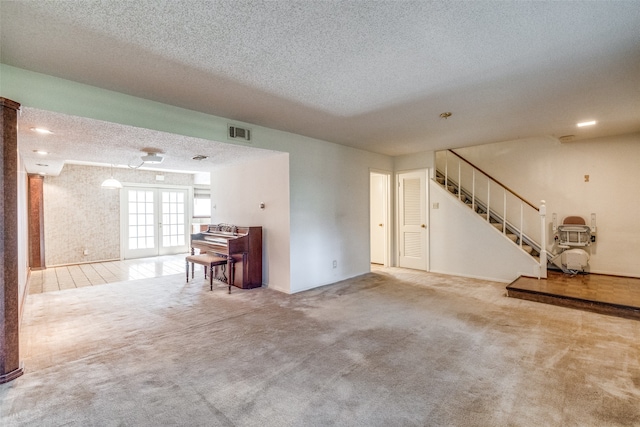 unfurnished living room with french doors, light colored carpet, and a textured ceiling