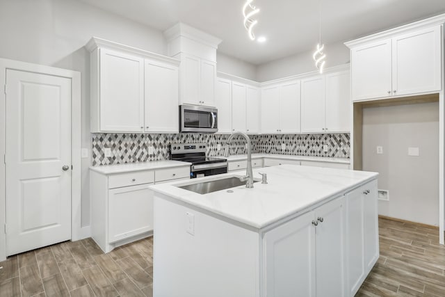 kitchen with appliances with stainless steel finishes, a center island with sink, light hardwood / wood-style floors, and white cabinets