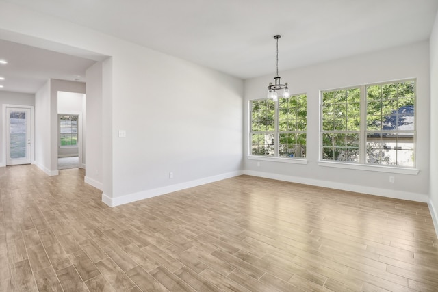 spare room featuring a notable chandelier, light wood-type flooring, and a wealth of natural light