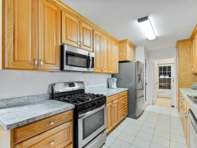 kitchen with a textured ceiling, sink, stainless steel appliances, light tile patterned floors, and light stone countertops