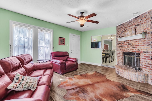 living room with a fireplace, hardwood / wood-style floors, a textured ceiling, and ceiling fan with notable chandelier