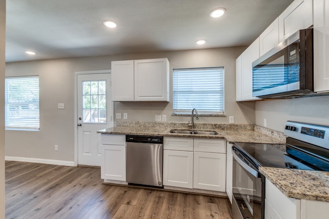 kitchen with sink, white cabinetry, appliances with stainless steel finishes, light stone countertops, and light hardwood / wood-style floors