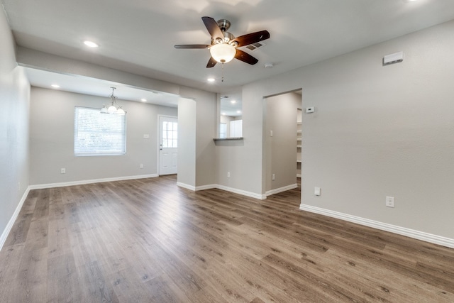 empty room with ceiling fan with notable chandelier and hardwood / wood-style flooring