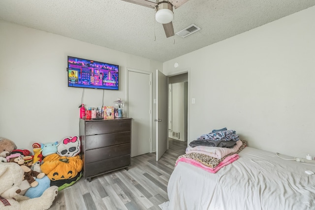 bedroom featuring light hardwood / wood-style floors, ceiling fan, and a textured ceiling