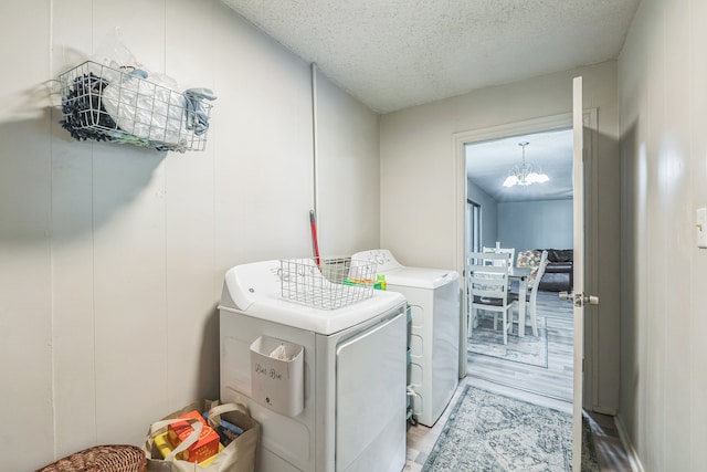 washroom with a textured ceiling, washer and clothes dryer, light hardwood / wood-style flooring, and a notable chandelier