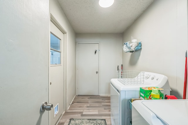 clothes washing area featuring a textured ceiling, light hardwood / wood-style floors, and washer and dryer