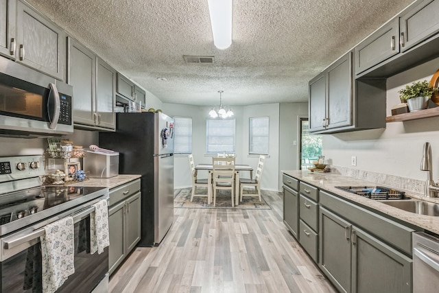 kitchen with pendant lighting, light hardwood / wood-style floors, sink, an inviting chandelier, and appliances with stainless steel finishes