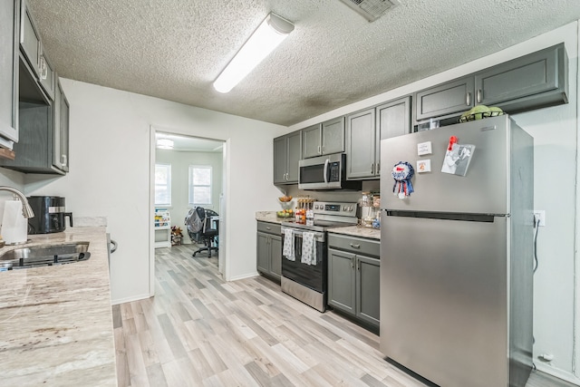 kitchen featuring light wood-type flooring, light stone counters, a textured ceiling, sink, and appliances with stainless steel finishes