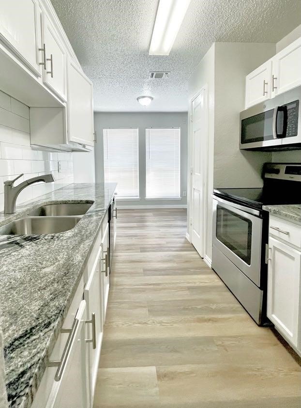 kitchen with light stone counters, sink, white cabinetry, light hardwood / wood-style flooring, and stainless steel appliances