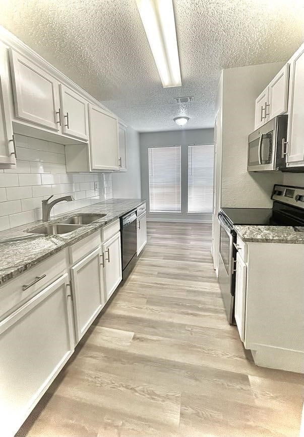 kitchen with light stone counters, sink, white cabinetry, stainless steel appliances, and light wood-type flooring