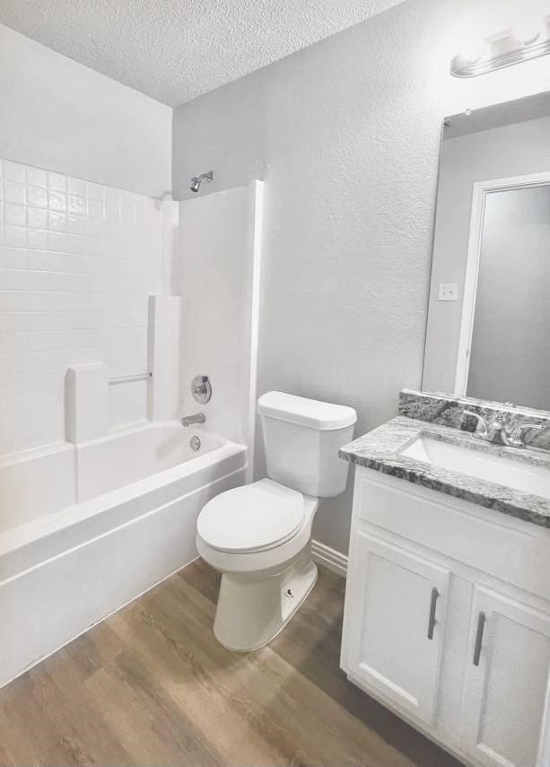 full bathroom with vanity, a textured ceiling, hardwood / wood-style flooring, shower / bathing tub combination, and toilet