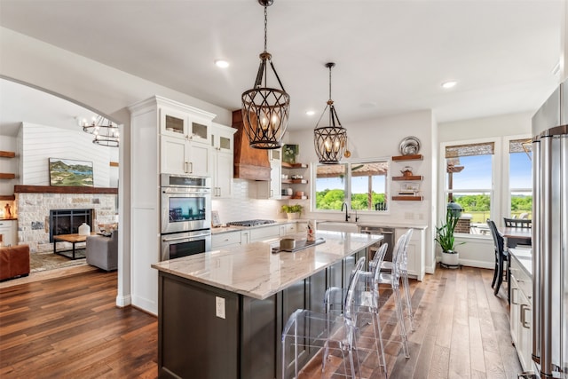 kitchen featuring dark wood-type flooring, white cabinetry, a kitchen island, decorative light fixtures, and a stone fireplace