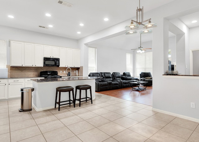 kitchen with white cabinets, a center island with sink, ceiling fan with notable chandelier, and black appliances