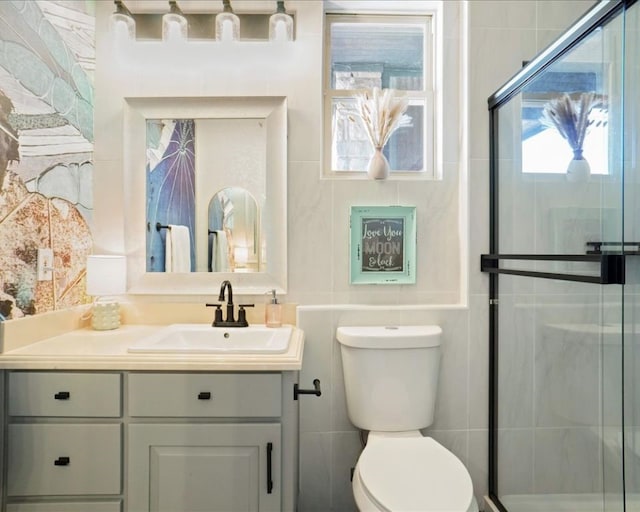 bathroom with tile walls, a shower with shower door, vanity, and toilet