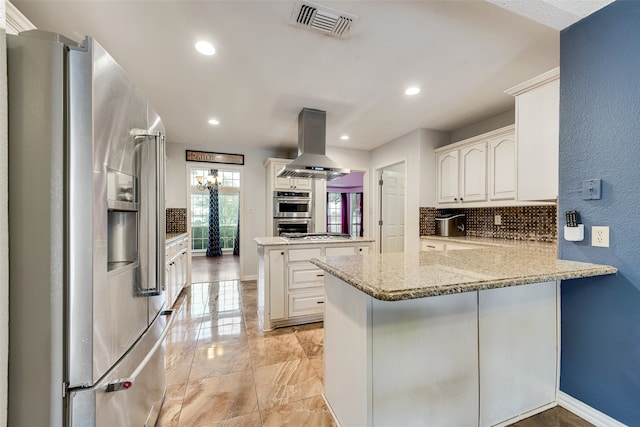 kitchen with appliances with stainless steel finishes, white cabinetry, kitchen peninsula, light stone countertops, and island exhaust hood