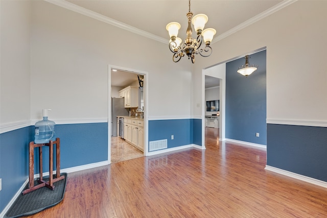 spare room with light wood-type flooring, crown molding, sink, and a notable chandelier