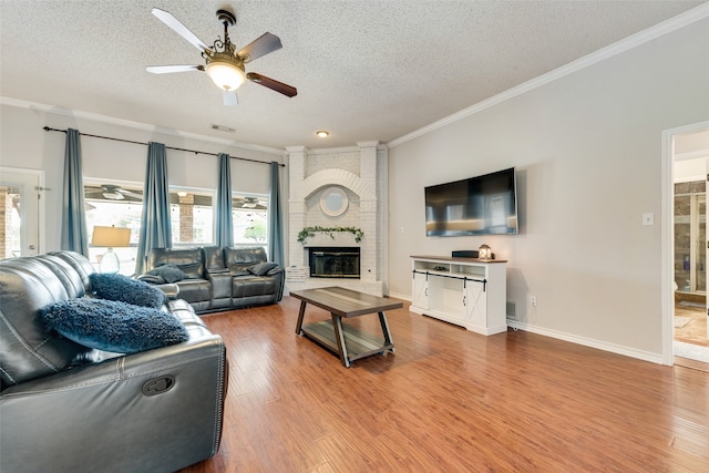 living room featuring a brick fireplace, ceiling fan, hardwood / wood-style floors, and a textured ceiling