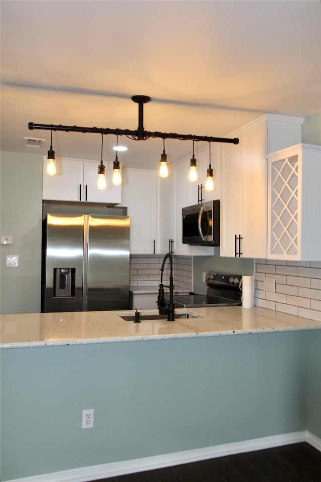 kitchen featuring white cabinets, backsplash, appliances with stainless steel finishes, and hanging light fixtures