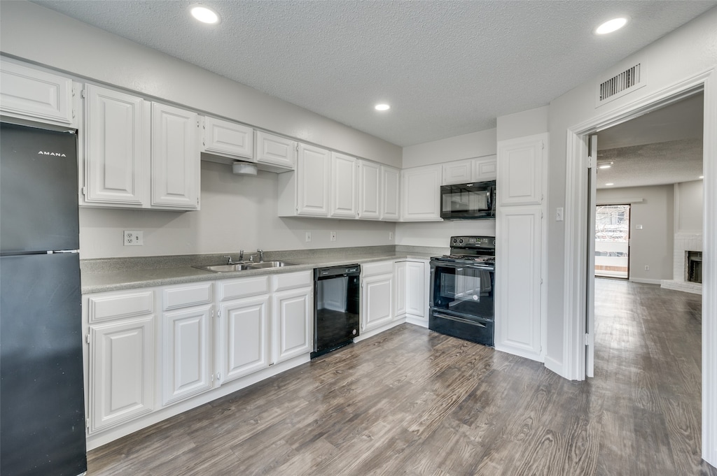 kitchen with white cabinetry, hardwood / wood-style flooring, a textured ceiling, black appliances, and sink